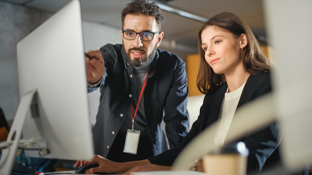 Business mentor helps scholar with project, advising on their work. Teacher giving lesson to diverse multiethnic group in college room, teaching new academic skills on a computer