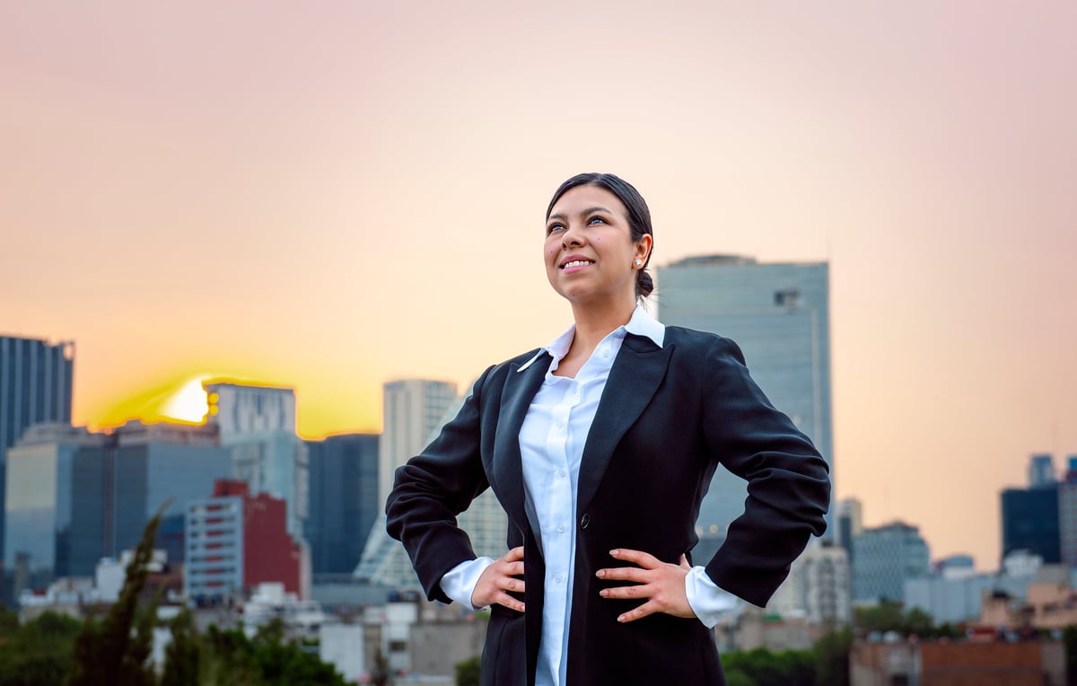 In the backdrop of corporate skyscrapers at sunset, a young, brown-haired Latina woman exudes success and empowerment in her executive suit. Her confident demeanor speaks of triumph and victory within the corporate world, showcasing her as a triumphant figure of empowerment and success.