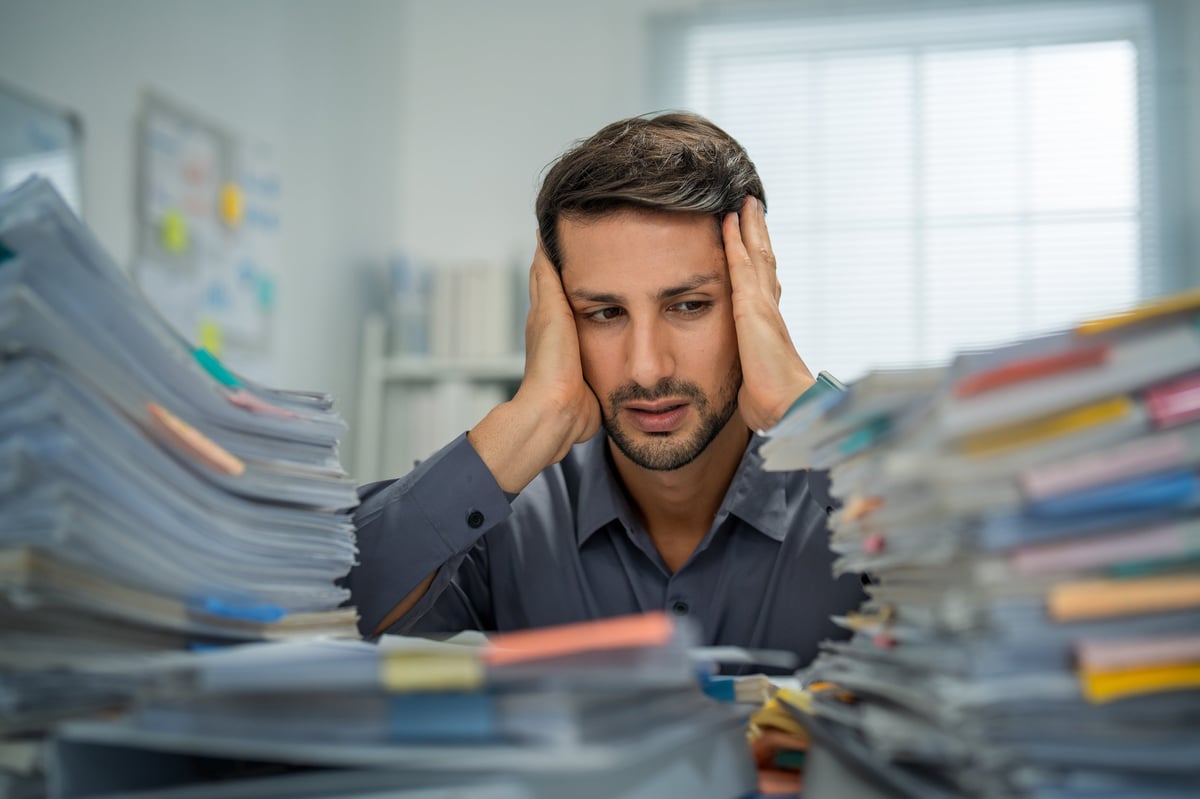 Hispanic male professional feeling deep fatigue and anxiety, overwhelmed by paperwork and deadlines, seeking help for burnout and emotional distress.