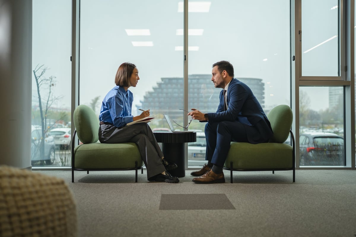 Two diverse professionals in a modern office engaged in a serious interview or meeting, one speaking intently while the other listens and takes notes, emphasizing communication and teamwork