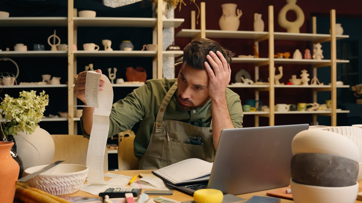 Shocked frustrated Caucasian man male small business owner potter gut businessman examining large bill check receipt debt bankruptcy shock payment problem unpaid tax accounting laptop in pottery store.