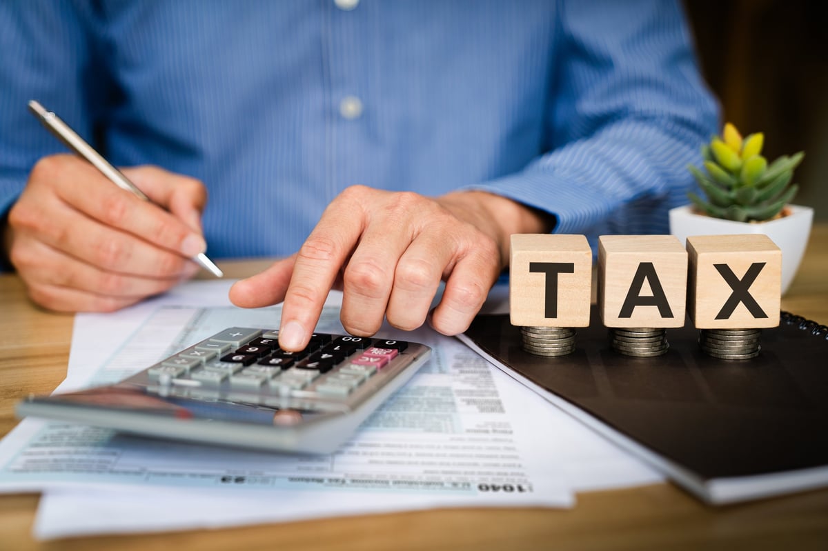 Business professional calculating tax with calculator and pen on financial documents, wooden TAX blocks on desk, illustrating income tax planning, accounting calculation, and finance preparation