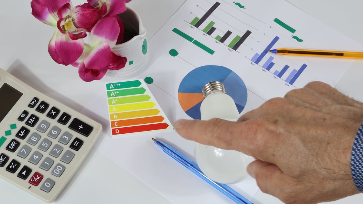 Green light bulb on desk with energy consumption graph. Detail of electricity bill with light bulb.