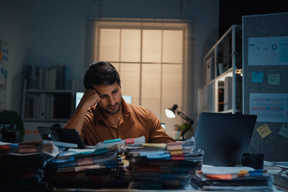 Stressed young Latin businessman having severe headache and migraine at desk in night office. Debt crisis, corporate burnout, late overtime workload, mental health anxiety, business failure concept.